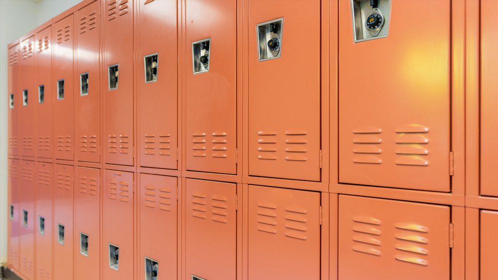 Light orange to pink, salmon color metal locker along a nondescript hallway in a typical US High School.